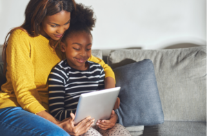 Mother and elementary school aged child sitting on a couch looking at a tablet together