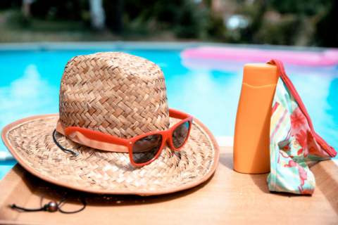 Poolside table with straw sunhat, sunglasses and sunscreen on it.