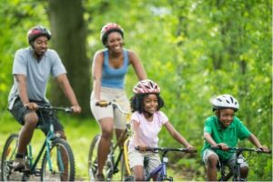 A mom, dad, and two young kids biking on a tree-lined path
