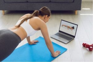 A woman in exercise clothing following along with a fitness video on her computer